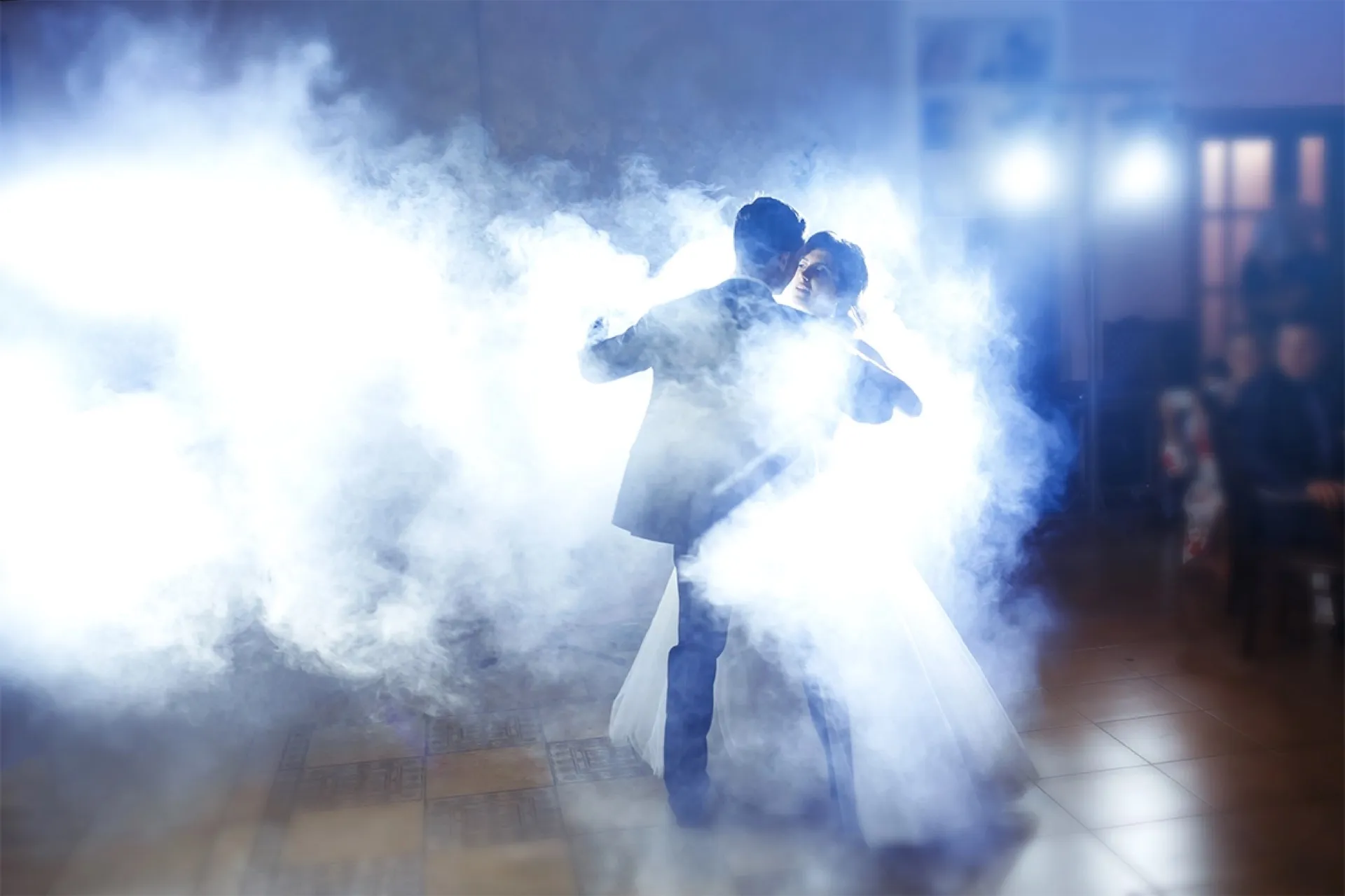 Bride and groom sharing their first dance in dramatic blue-lit smoke
